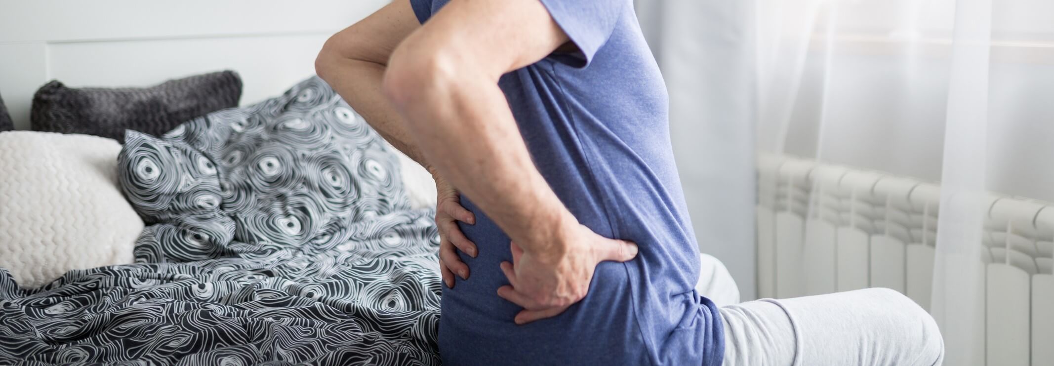 An old man sitting on bed experiencing a lumbar spasm