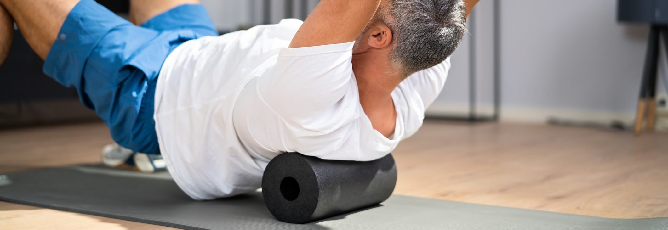 Young mascular man massaging his upper back with a foam roller
